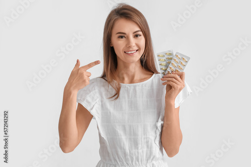 Beautiful woman pointing at blisters of vitamin supplements on grey background