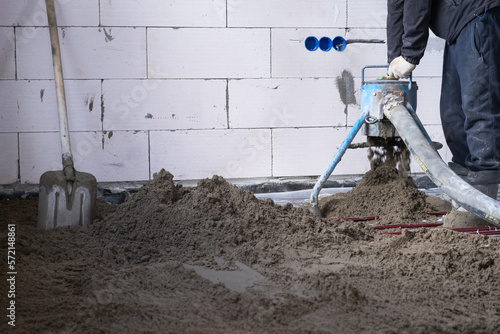 Semi-dry floor screed - a worker shovels a construction mixture through a special sleeve for cementing and leveling on underfloor heating pipes.