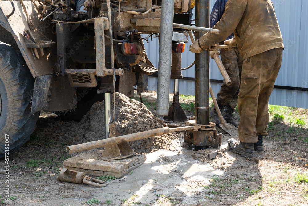 Team of workers with drilling rig on car are drilling artesian well for