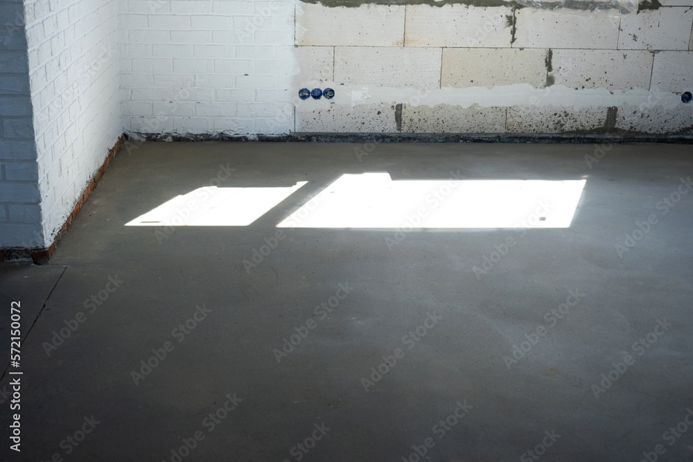 The leveled rough floor in a house under construction with a semi-dry cement screed is a smooth surface with light from the windows The leveled rough floor in a house under construction with a semi-dry cement screed is a smooth surface with light from the windows