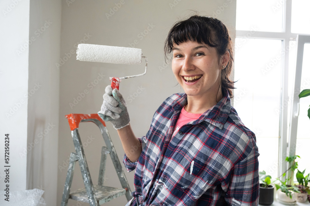 Happy woman in paint roller and white paint for walls in hands close-up portrait. Construction work and cosmetic repairs in house, wall painting, tinting, finishing work with your own hands Happy woman in paint roller and white paint for walls in hands close-up portrait. Construction work and cosmetic repairs in house, wall painting, tinting, finishing work with your own hands