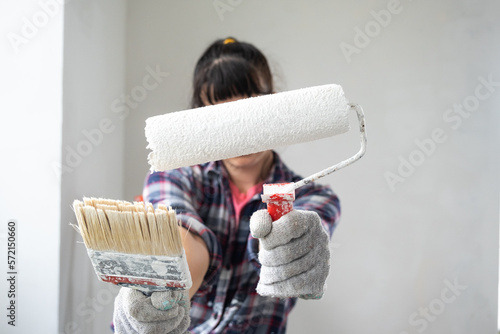 Happy woman in paint roller and white paint for walls in hands close-up portrait. Construction work and cosmetic repairs in house, wall painting, tinting, finishing work with your own hands