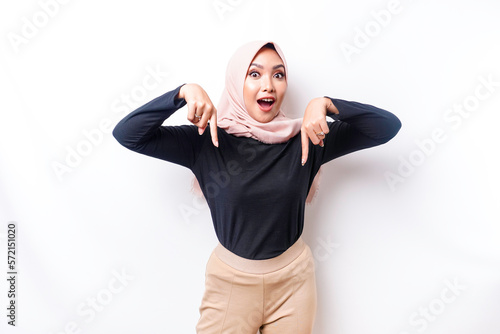 Shocked Asian Muslim woman wearing hijab pointing at the copy space below her, isolated by white background © Reezky