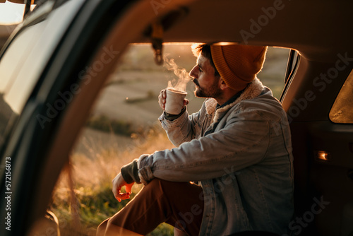 A man sits in the trunk of a car and drinks a fresh hot coffee by himself. Travel alone concept photo