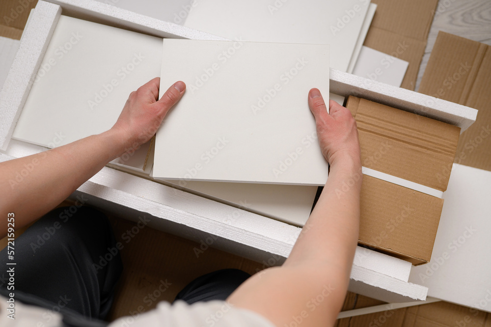 Man unpacking boxes with furniture boards for furniture assembly. Unpacking cardboard boxes after moving house. Man unpacking boxes with furniture boards for furniture assembly. Unpacking cardboard boxes after moving house.