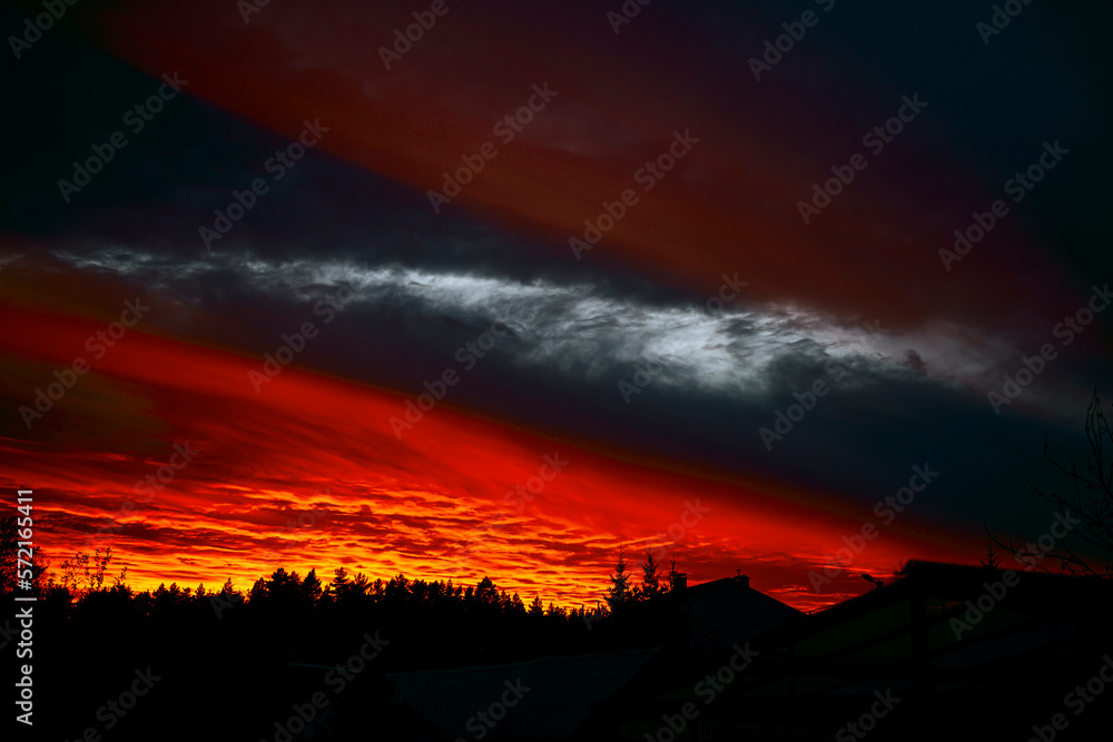 A red sunset breaking through the thickness of blackness. A fiery sunset over the roofs of houses.Impressive sky background.Mysticism.Or war, terror, the concept of the struggle of light with darkness