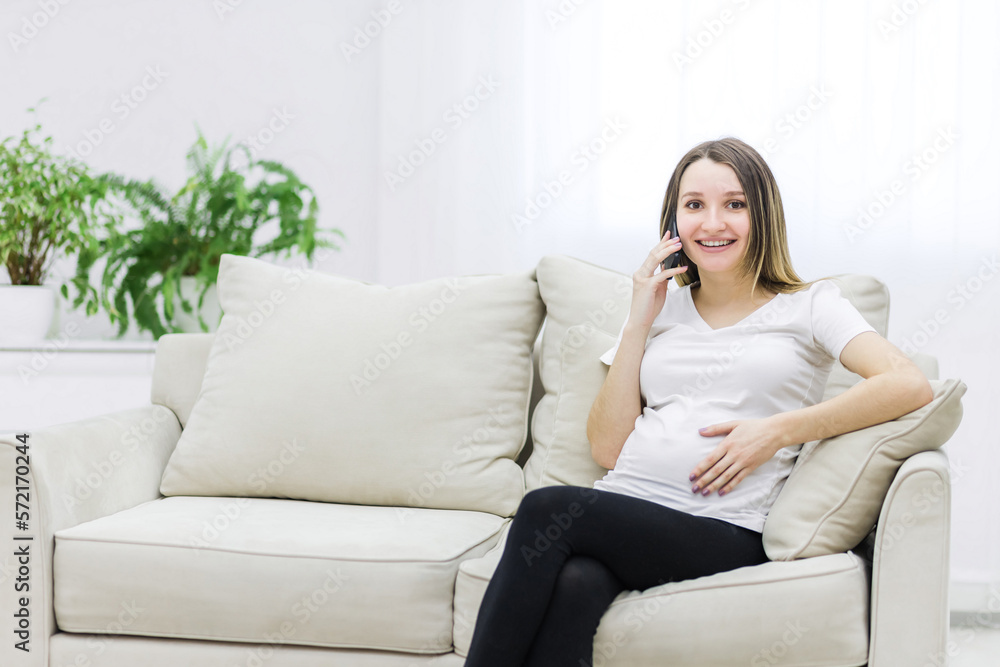 Smiling pregnant woman talking over the phone on white sofa. Smiling pregnant woman talking over the phone on white sofa.