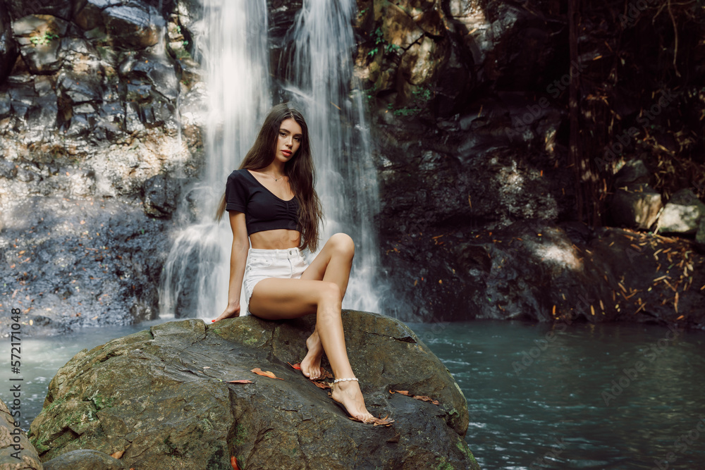 Beautiful young woman posing on waterfall in Bali