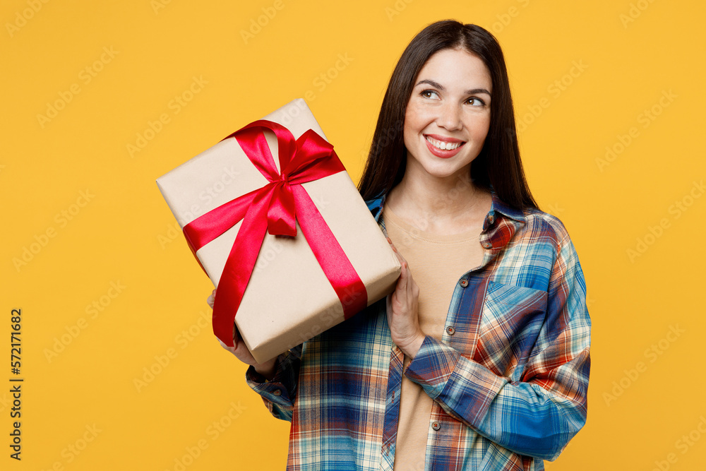 Young minded wistful woman wear blue shirt beige t-shirt present box with gift ribbon bow look aside on workspace area isolated on plain yellow background studio portrait. People lifestyle concept. Young minded wistful woman wear blue shirt beige t-shirt present box with gift ribbon bow look aside on workspace area isolated on plain yellow background studio portrait. People lifestyle concept.