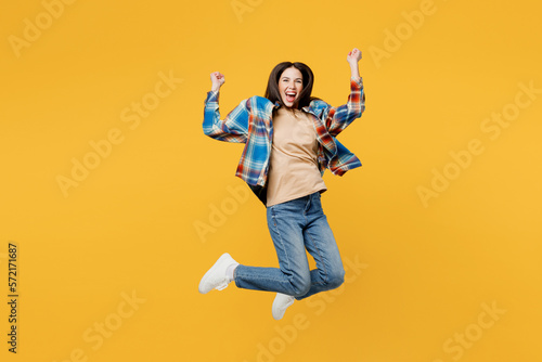 Full body young excited happy fun overjoyed woman wear blue shirt beige t-shirt jump high do winner gesture clench fists isolated on plain yellow background studio portrait. People lifestyle concept.