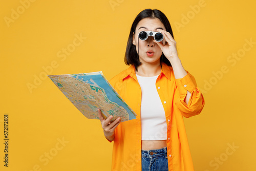 Young amazed woman in summer casual clothes hold in hand map use binoculars isolated on plain yellow background. Tourist travel abroad in free spare time rest getaway Air flight trip journey concept #572172081