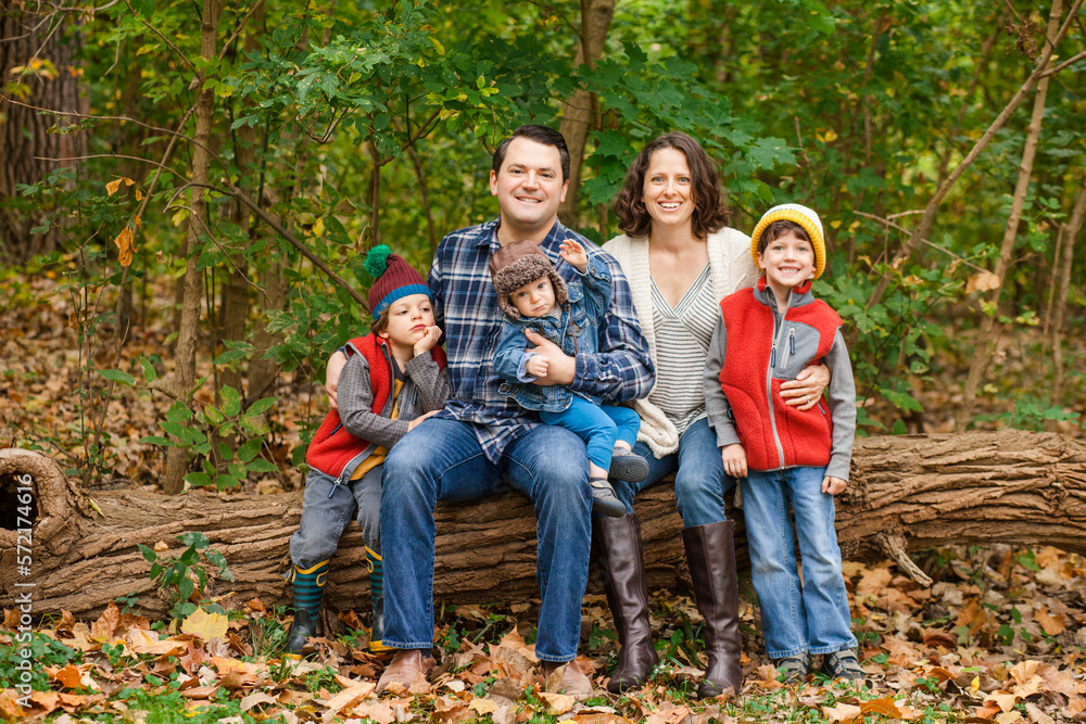 a smiling family sit together on a log in the woods a smiling family sit together on a log in the woods