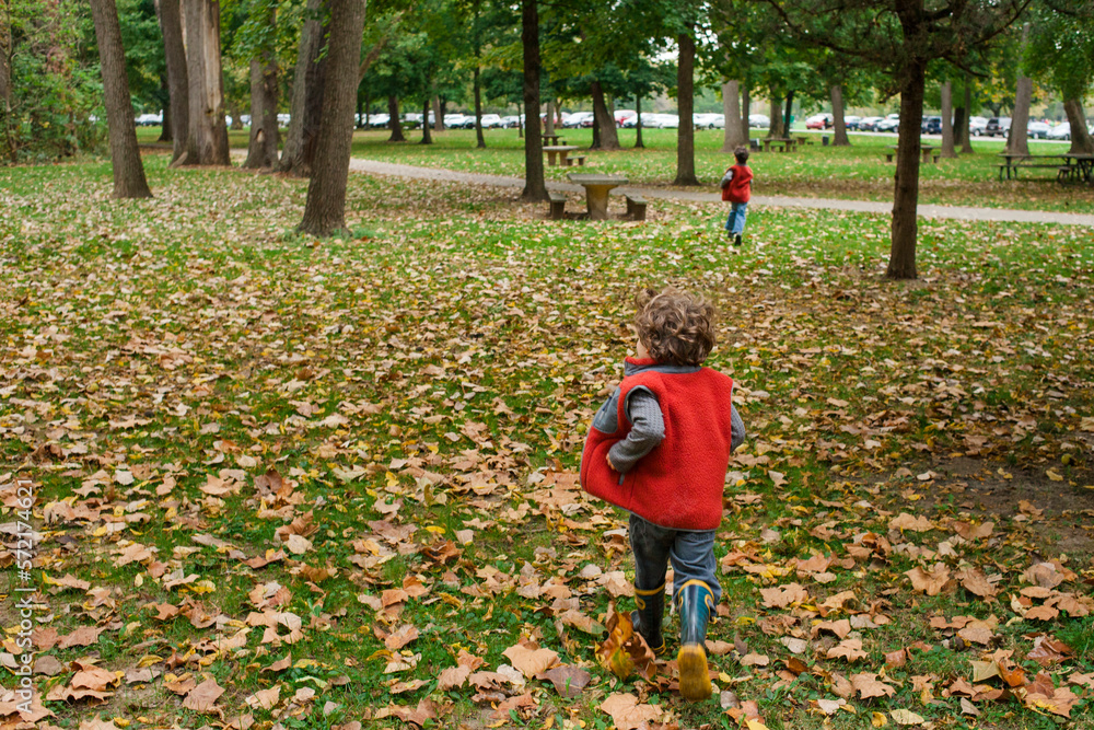 two small children run together through fallen leaves in a park two small children run together through fallen leaves in a park