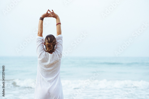 Woman with her back and white dress doing stretching on the beach. photo