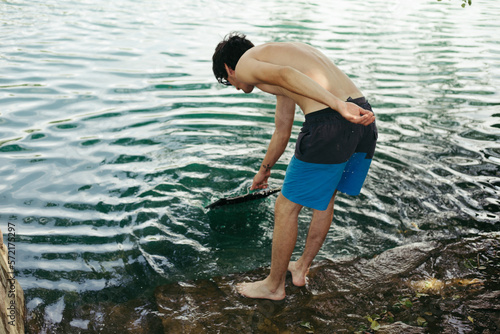 Young man in beach shorts washing grill in a river photo