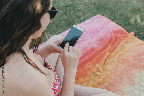 Girl sitting on a towel with mobile phone on the lawn of the pool III photo