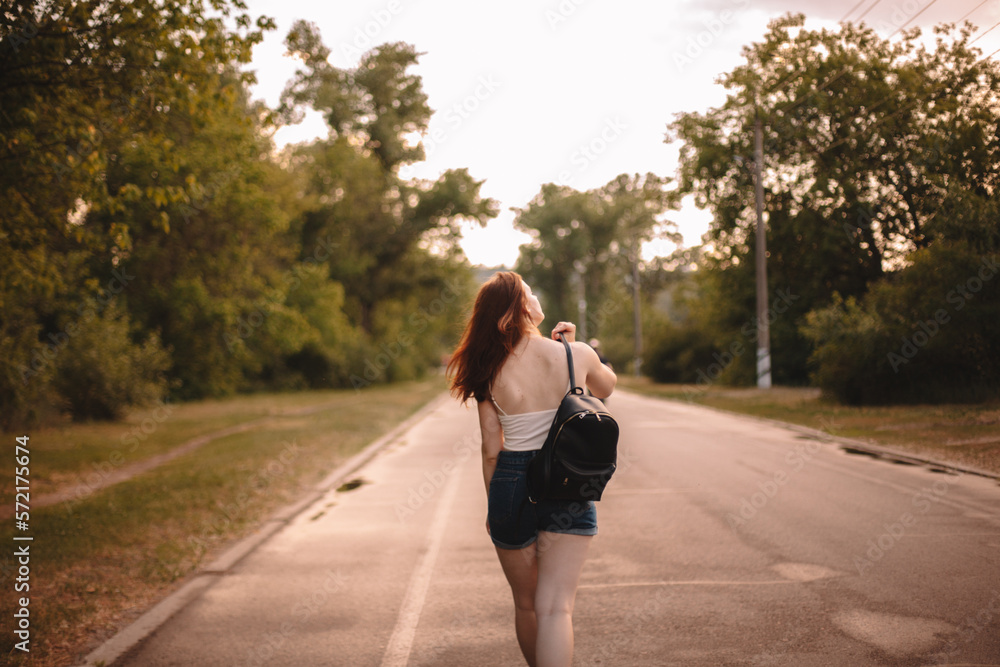 Rear view of young woman walking on country road during summer Rear view of young woman walking on country road during summer