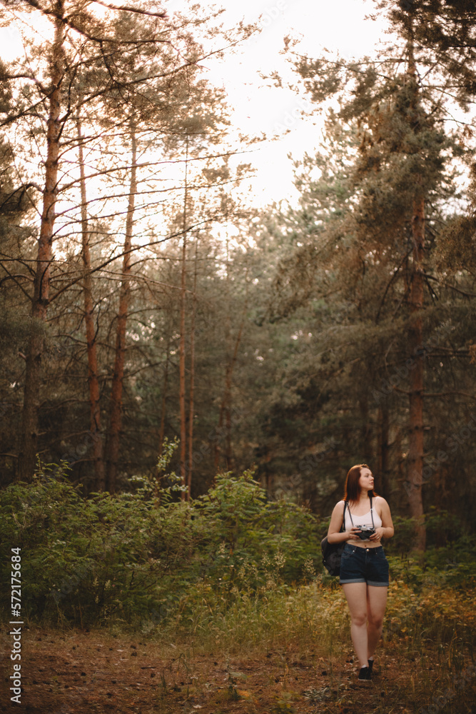 Female hiker with camera walking in forest during summer Female hiker with camera walking in forest during summer