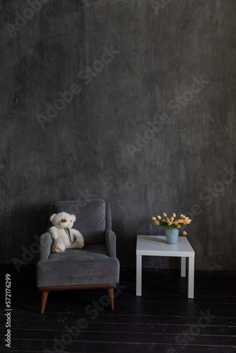 armchair with soft toy and table with flowers in the interior