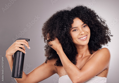 Face of black woman spray product on hair for natural wellness, growth and shine on gray background. Beauty, luxury salon and happy girl smile with hairspray, cosmetic products and keratin treatment