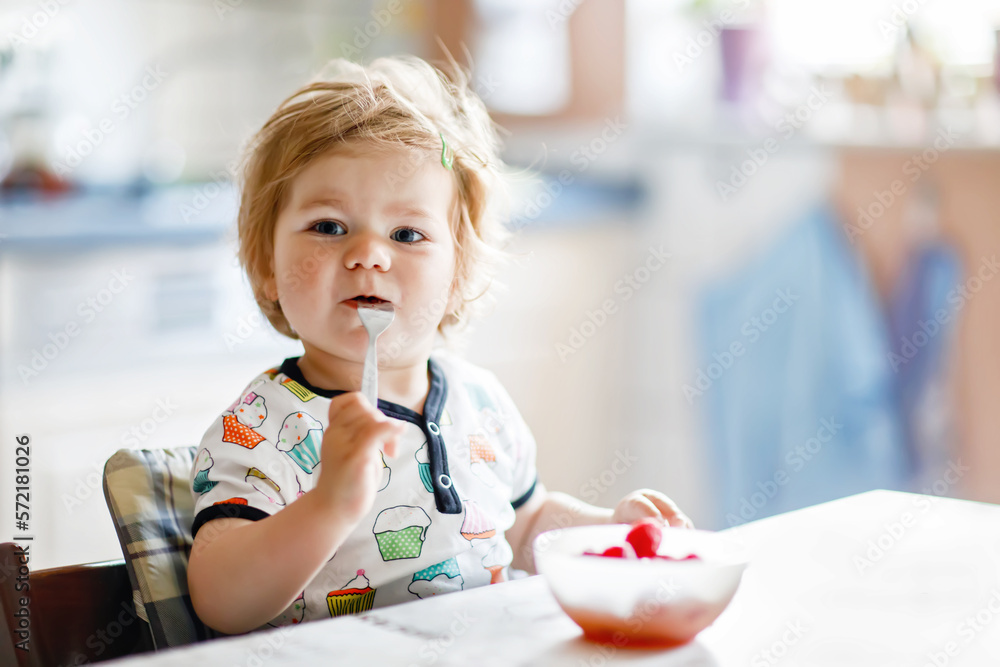 Adorable baby girl eating from spoon fresh healthy raspberries food, child, feeding and development concept. Cute toddler, daughter with spoon sitting in highchair and learning to eat by itself. Adorable baby girl eating from spoon fresh healthy raspberries food, child, feeding and development concept. Cute toddler, daughter with spoon sitting in highchair and learning to eat by itself.