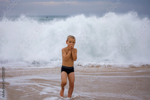 Little boy plays on the shore of a huge raging ocean. He joyfully runs away from the waves. Freedom, security, childhood. Challenge, adventure and travel photo