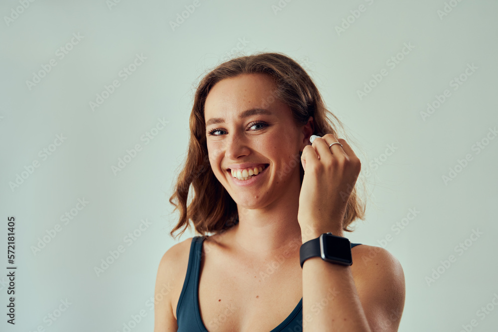 Portrait of young caucasian woman with fitness tracker smiling while putting in wireless headphones Portrait of young caucasian woman with fitness tracker smiling while putting in wireless headphones