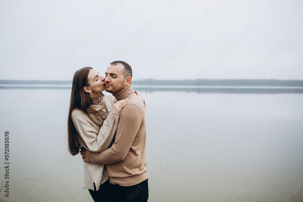 man and woman hugging on the lake shore, cold foggy weather. romantic photo in beige clothes. to hug a woman, a love story. beige sweaters. romantic photos against the background of a foggy lake