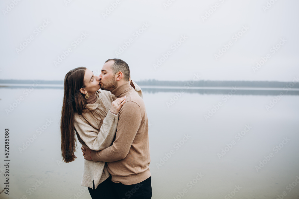 man and woman hugging on the lake shore, cold foggy weather. romantic photo in beige clothes. to hug a woman, a love story. beige sweaters. romantic photos against the background of a foggy lake