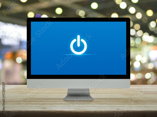 Power button icon on desktop modern computer monitor screen on wooden table over blur light and shadow of shopping mall, Business start up online concept