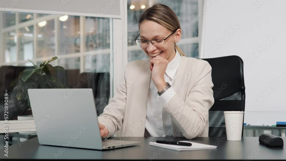 Young business woman manager in glasses and light formal suit sits at table with laptop working from office. Female CEO gets great online news puts hand on chin, satisfied successful entrepreneur. Young business woman manager in glasses and light formal suit sits at table with laptop working from office. Female CEO gets great online news puts hand on chin, satisfied successful entrepreneur.