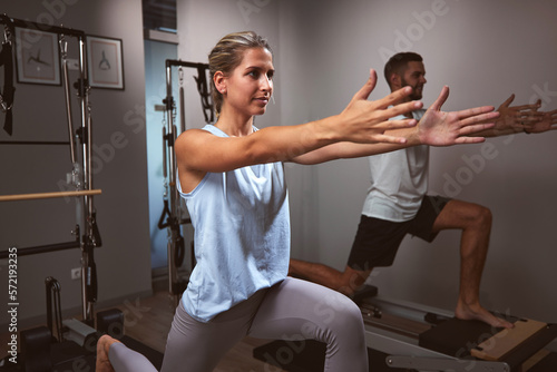 Young woman and man exercising in a gym with personal trainer on pilates machine.