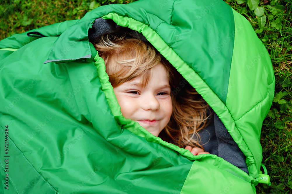 Preschool little girl in sleeping bag camping. Outdoors activity with children in summer. Fun