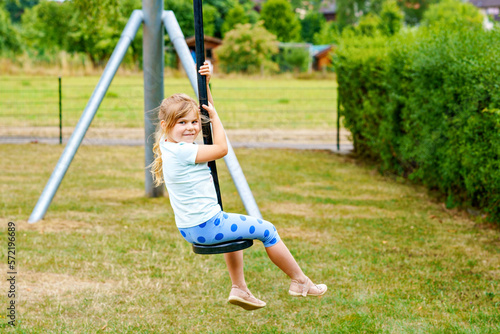 Happy kid girl rids on zip line swing outdoor game play equipment on playground. Child having fun outdoors. Preschool child swinging on summer day. Activity with children.