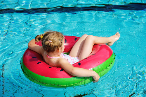 Happy little girl playing with colorful inflatable ring in outdoor swimming pool on sunny summer day. Preschool child learn to swim. Summer outdoor activity