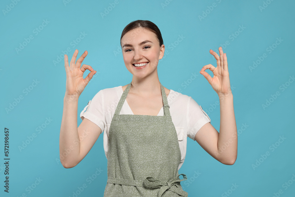 Beautiful young woman in clean apron with pattern on light blue background Beautiful young woman in clean apron with pattern on light blue background