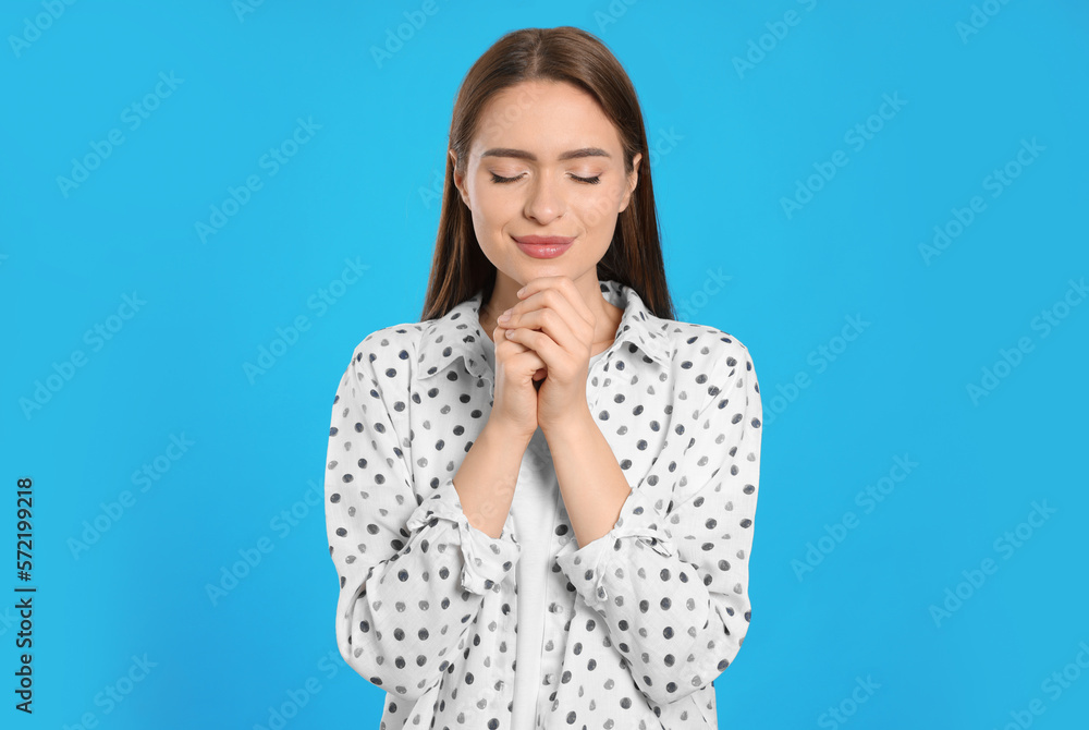 Woman with clasped hands praying on turquoise background
