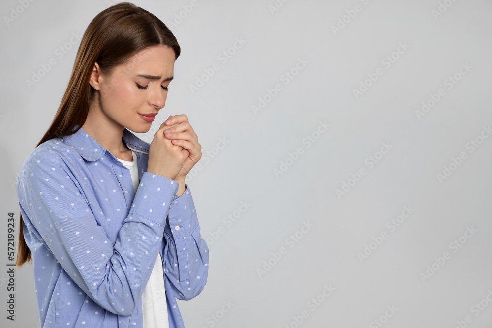 Woman with clasped hands praying on light grey background, space for text Woman with clasped hands praying on light grey background, space for text