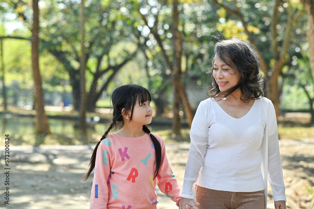Adorable little child and elderly grandmother walking in the park, spending time outdoor together. Family and love concept Adorable little child and elderly grandmother walking in the park, spending time outdoor together. Family and love concept