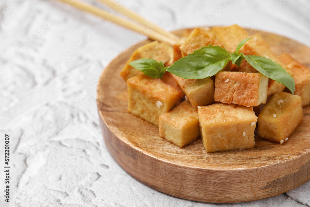 Wooden plate with delicious fried tofu, basil and sesame seeds on light grey table, closeup. Space for text