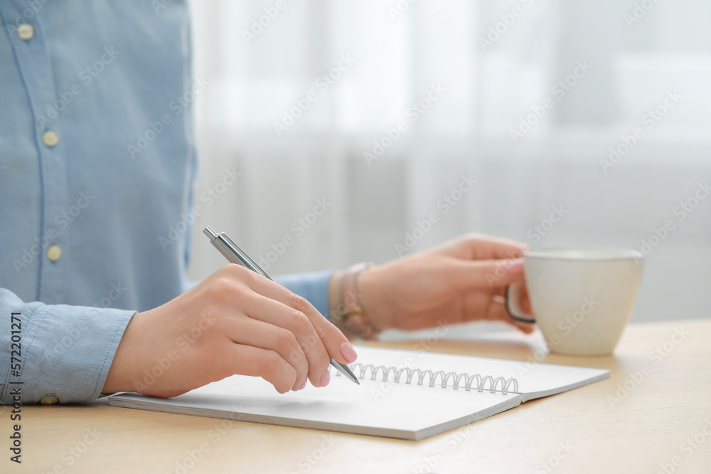 Woman writing in notebook at wooden table, closeup Woman writing in notebook at wooden table, closeup