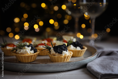 Canvastavla Delicious tartlets with red and black caviar served on white wooden table against blurred festive lights, closeup