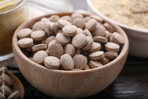 Brewer`s yeast tablets in bowl on wooden table, closeup