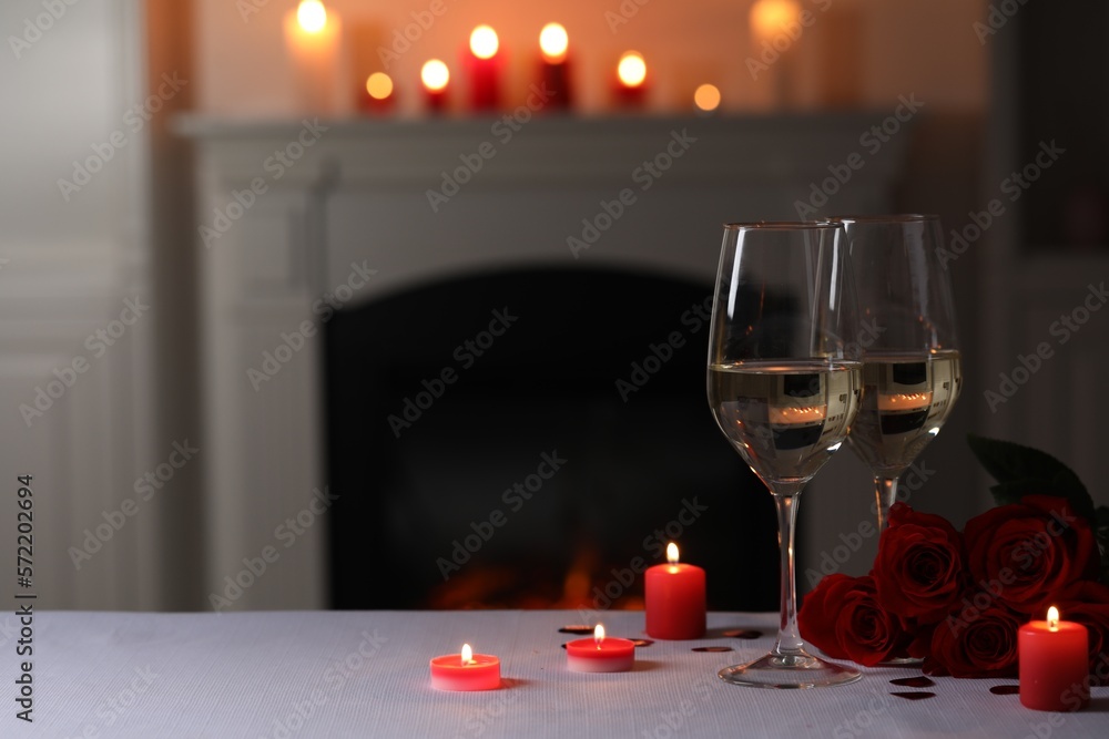 Glasses of white wine, rose flowers and burning candles on grey table indoors, space for text. Romantic atmosphere Glasses of white wine, rose flowers and burning candles on grey table indoors, space for text. Romantic atmosphere