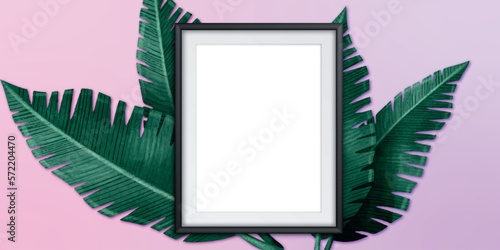 An empty white photo frame and green leaves are on a pastel coloreful concrete background. Floral layout. Flat lay. Top view. Copy space.