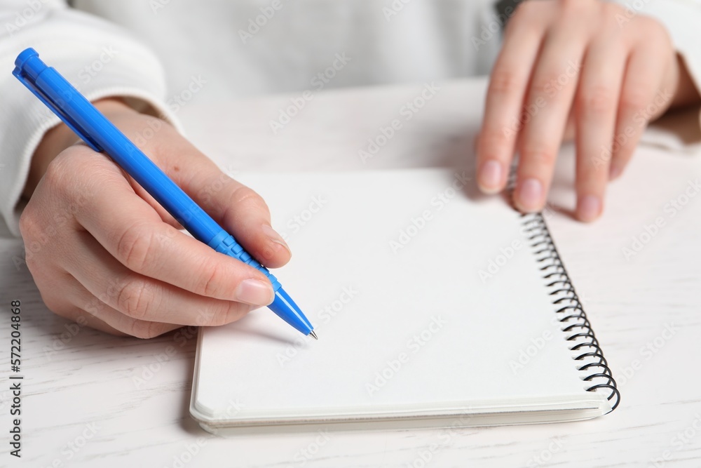 Woman writing in notebook with pen at white wooden table, closeup Woman writing in notebook with pen at white wooden table, closeup