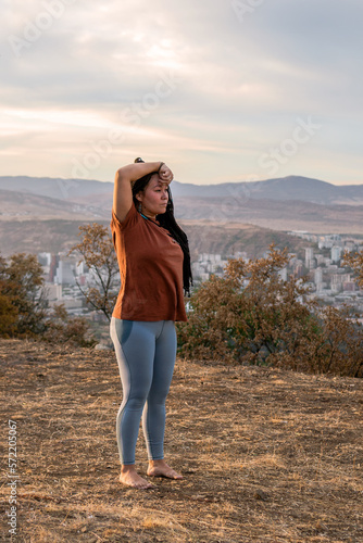 Portrait of beautiful European woman with long African braids. Woman is doing yoga exercise outside on background of mountains.