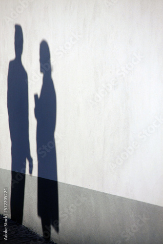 Shadow of two people on the wall, one holding a glass and the other holding her bag in her arms.