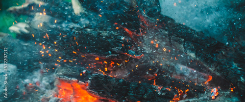 Vivid smoldered firewoods burned in fire closeup. Atmospheric background with orange flame of campfire. Full frame image of bonfire with sparks in bokeh. Warm vortex of glowing embers and ashes in air