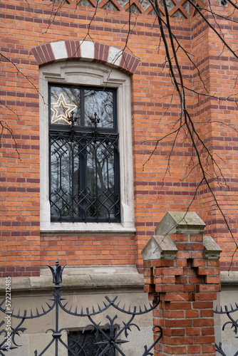 A window in the wall of a house made of multi-colored bricks with a beautiful forged lattice and fence elements.